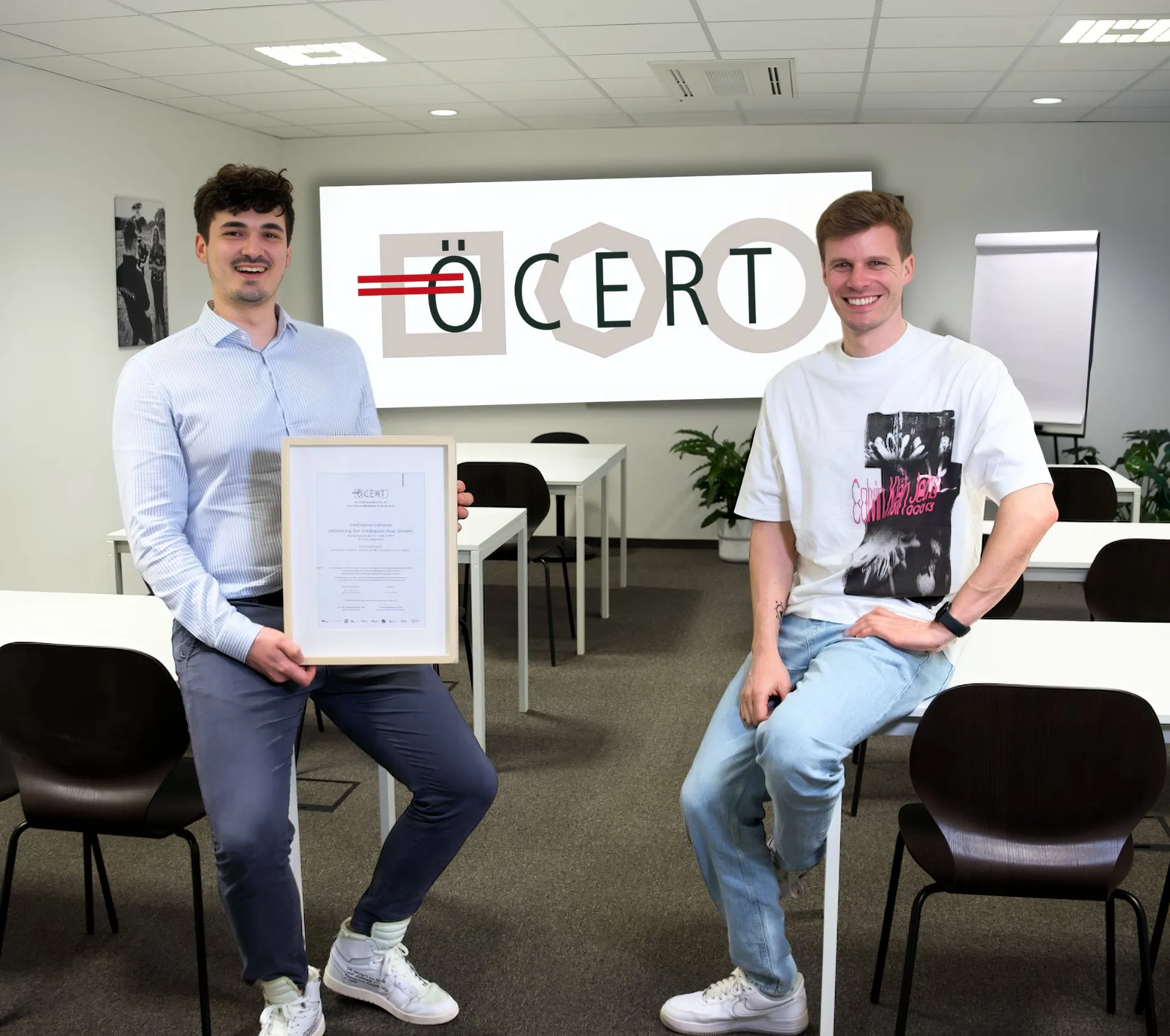 Zwei Kursteilnehmer mit ÖCERT-Zertifikat im mediapool campus Seminarraum; großes ÖCERT-Logo im Hintergrund