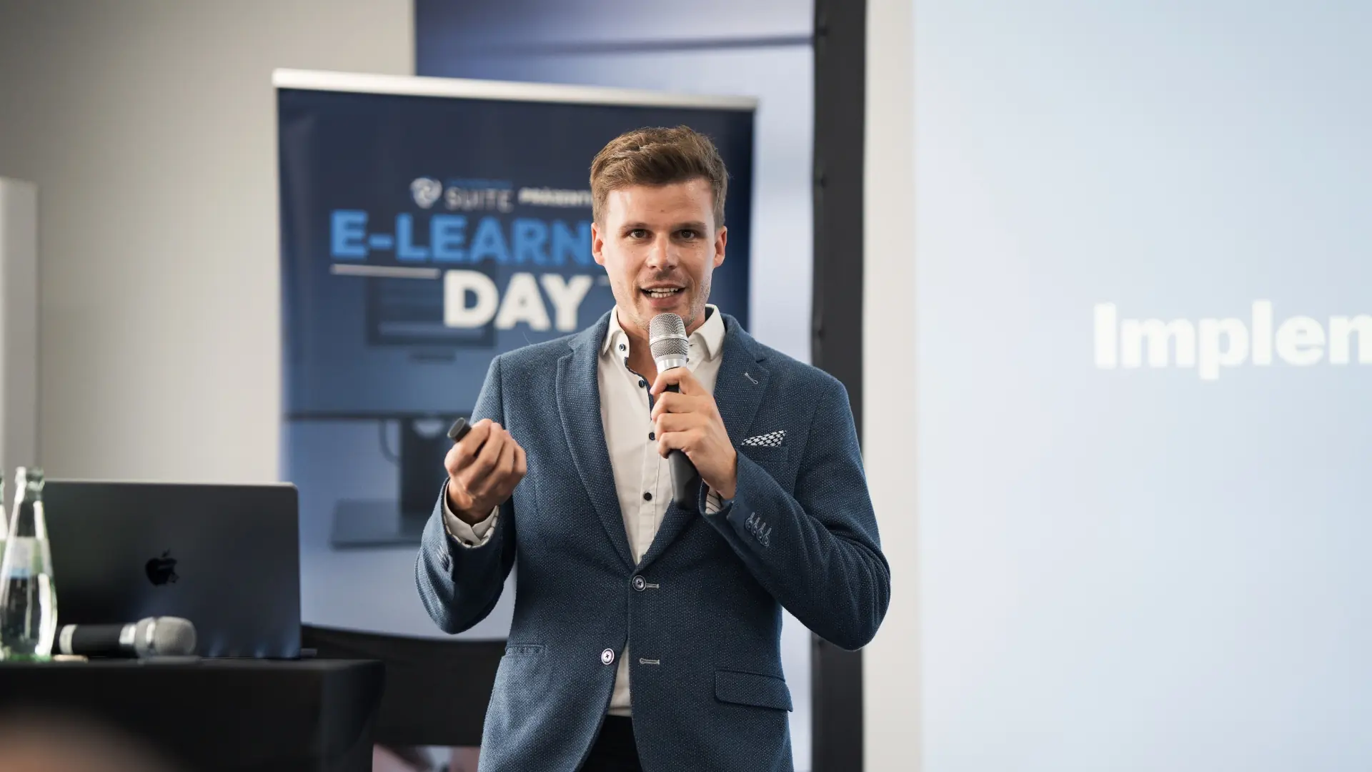 Keynote vor Publikum: Referent mit Mikrofon, Leinwand und E-Learning-Day-Banner