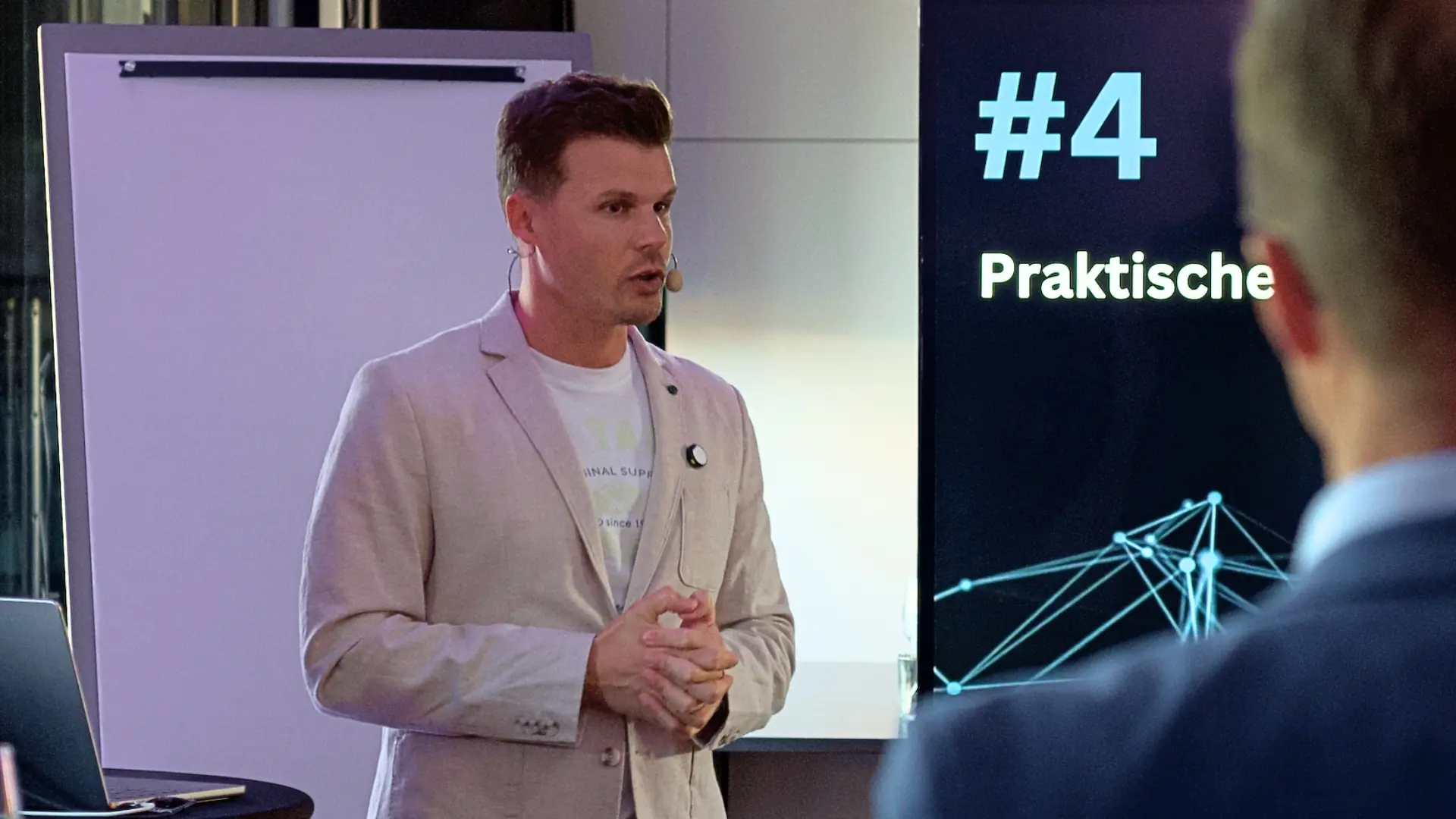 Impulsvortrag zu KI: Referent mit Headset vor Screen mit Präsentationsfolie und Netzwerkgrafik