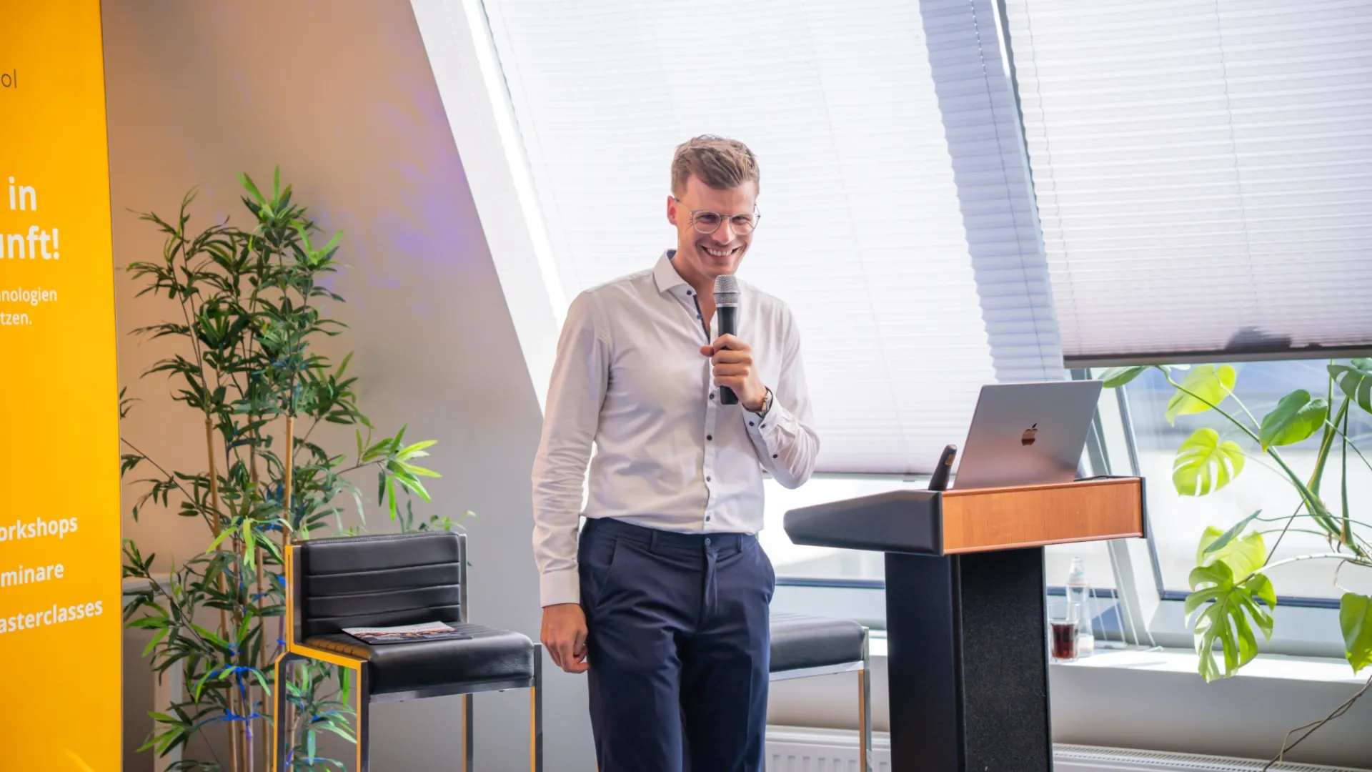 Referent mit Mikrofon und Laptop am Rednerpult in modernem Schulungsraum