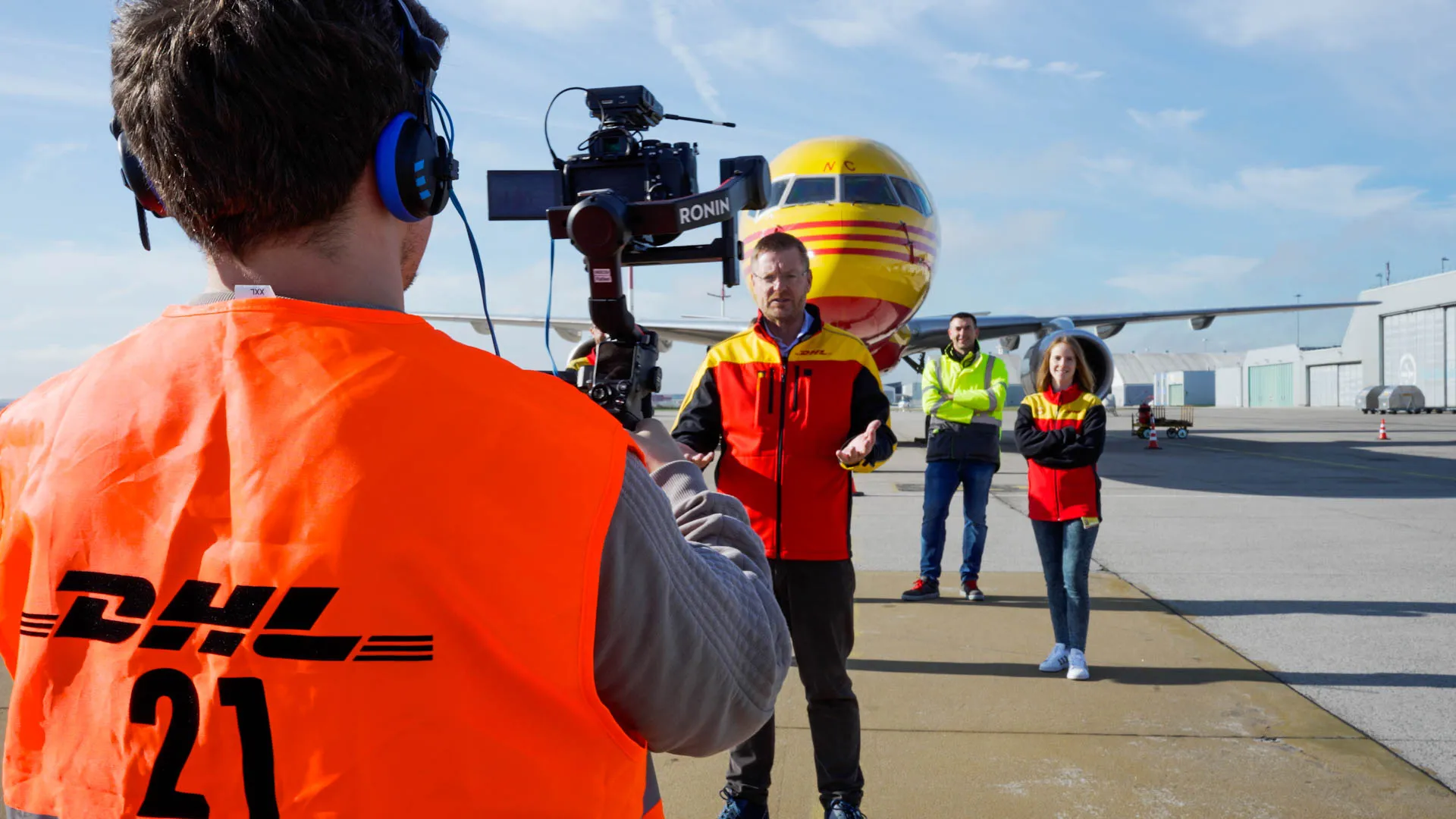 Videoproduktion am Flughafen: Kamera auf Gimbal, Interview vor DHL-Frachtflugzeug auf dem Vorfeld