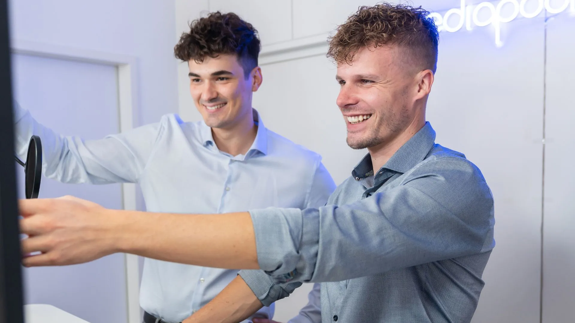 Zwei mediapool-Kolleginnen und Kollegen im hellen Büro mit mediapool-Leuchtschrift an der Wand